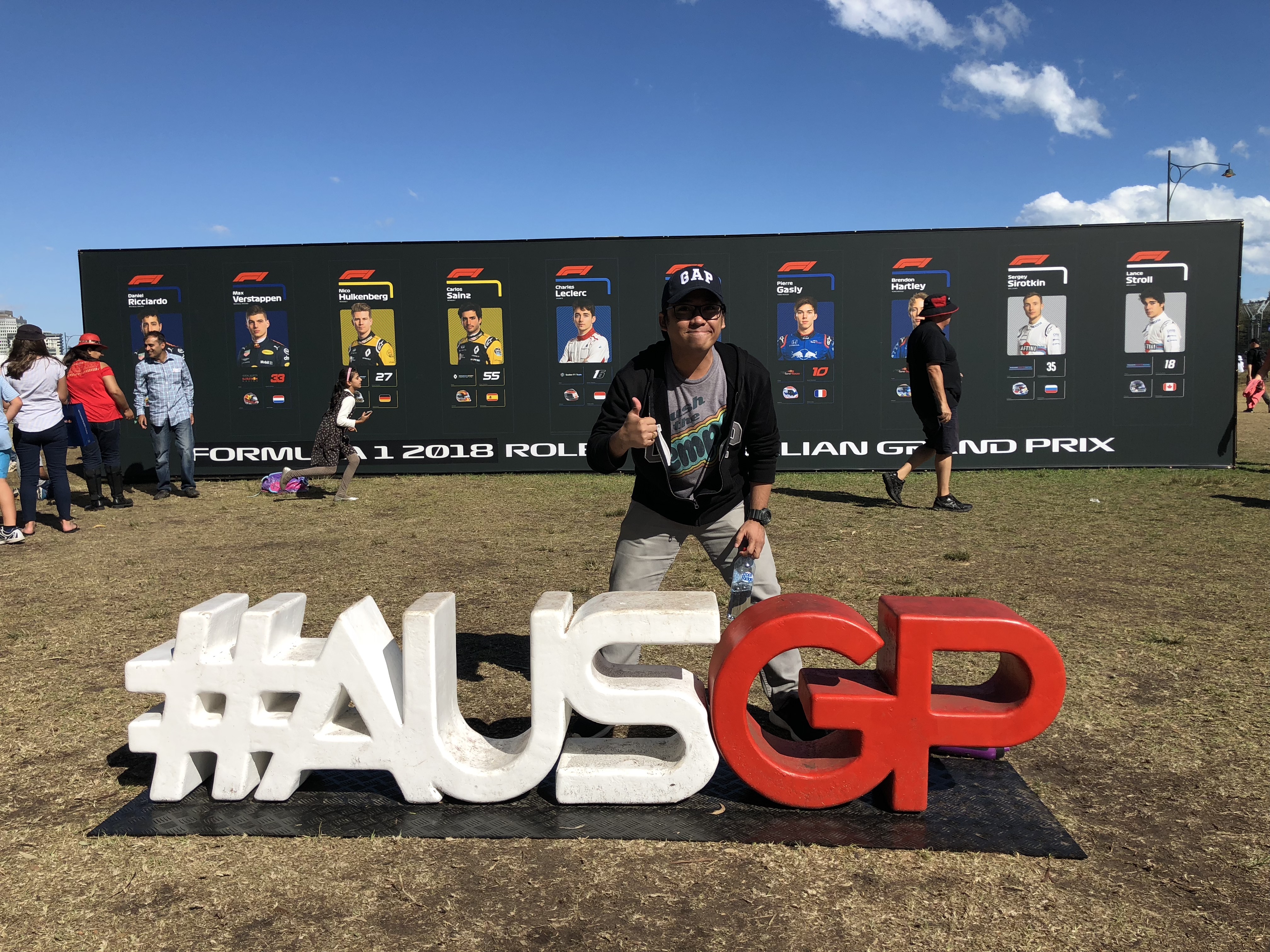 Dr Dennis John Sumaylo stands in front an AUSGP sign, with his thumbs up.
