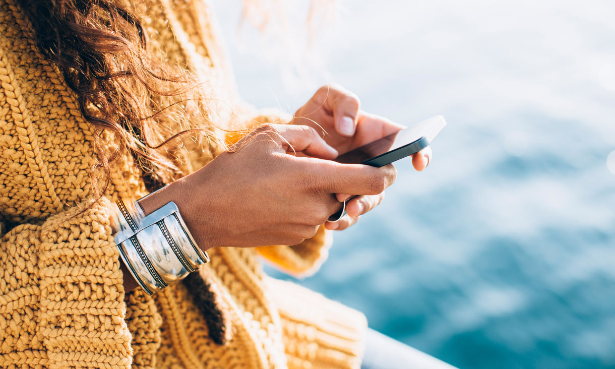 A person texting on their phone by the water.