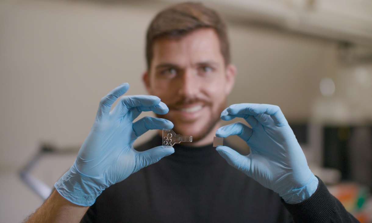 Dr Cesar Sanchez Huertas holding the two devices the project brings together - a microfluidic chip (right) and photonic biosensor (left).