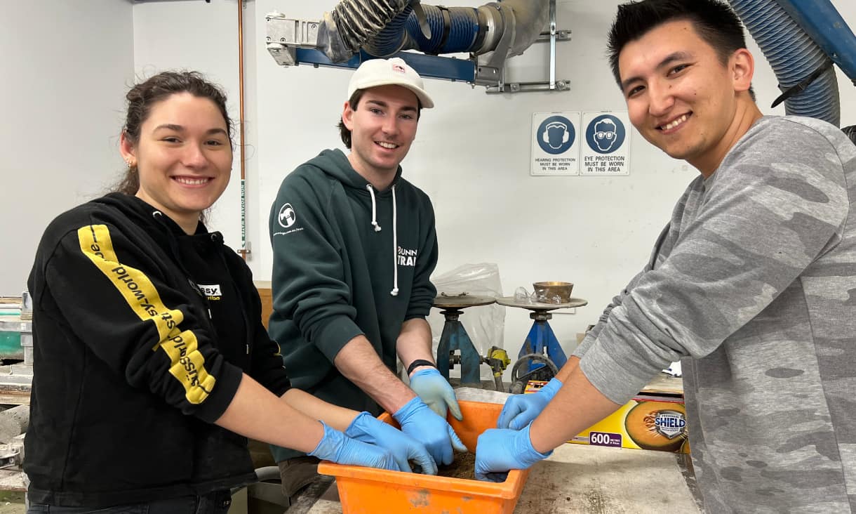 Three people mixing soil in an orange bucket in a lab