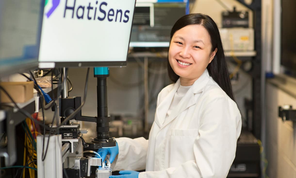a woman using a microscope and smiling at the camera