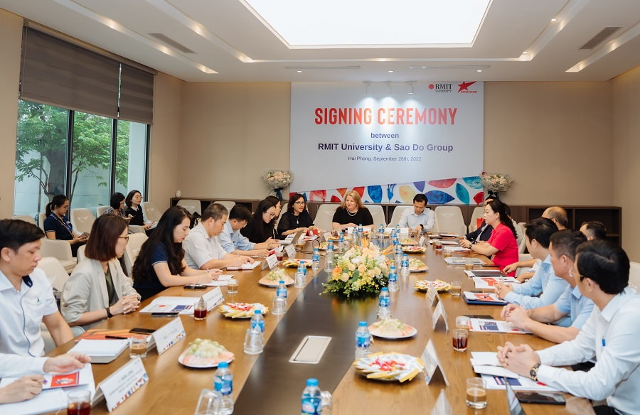 The members of each group sit on a long table listening to the leaders speak