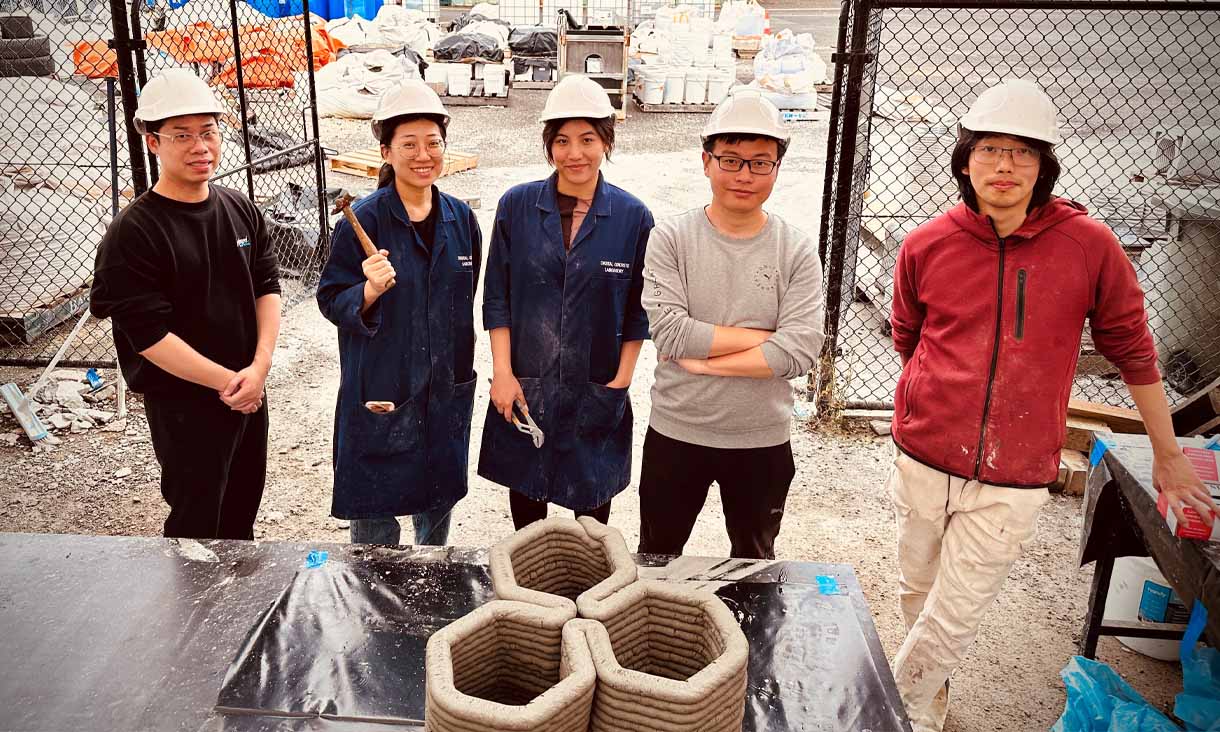 RMIT students wearing navy lab coats and hard hats with their 3D printed structure.