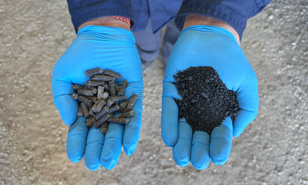 Feedstock from a waste stream is in the left blue gloved hand and a carbon-rich product called biochar is in the other blue gloved hand.