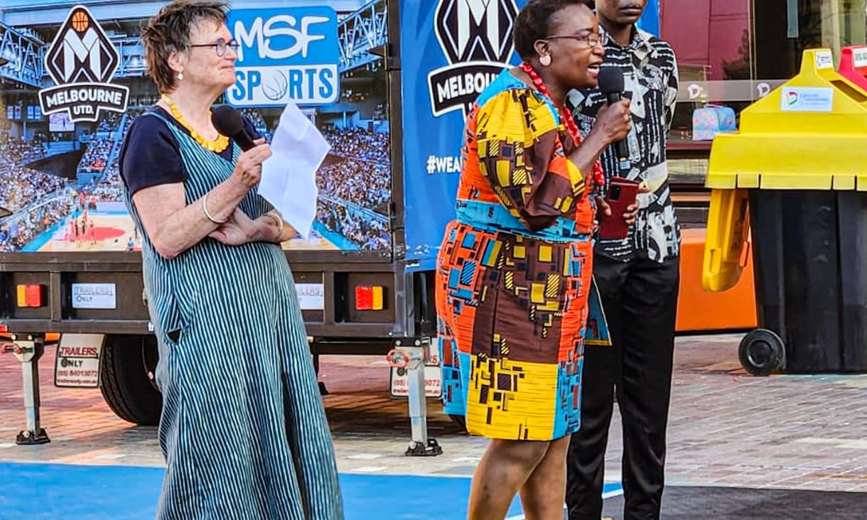 Ronnie Egan and Selba-Gondoza Luka standing outside, Selba speaking into a microphone