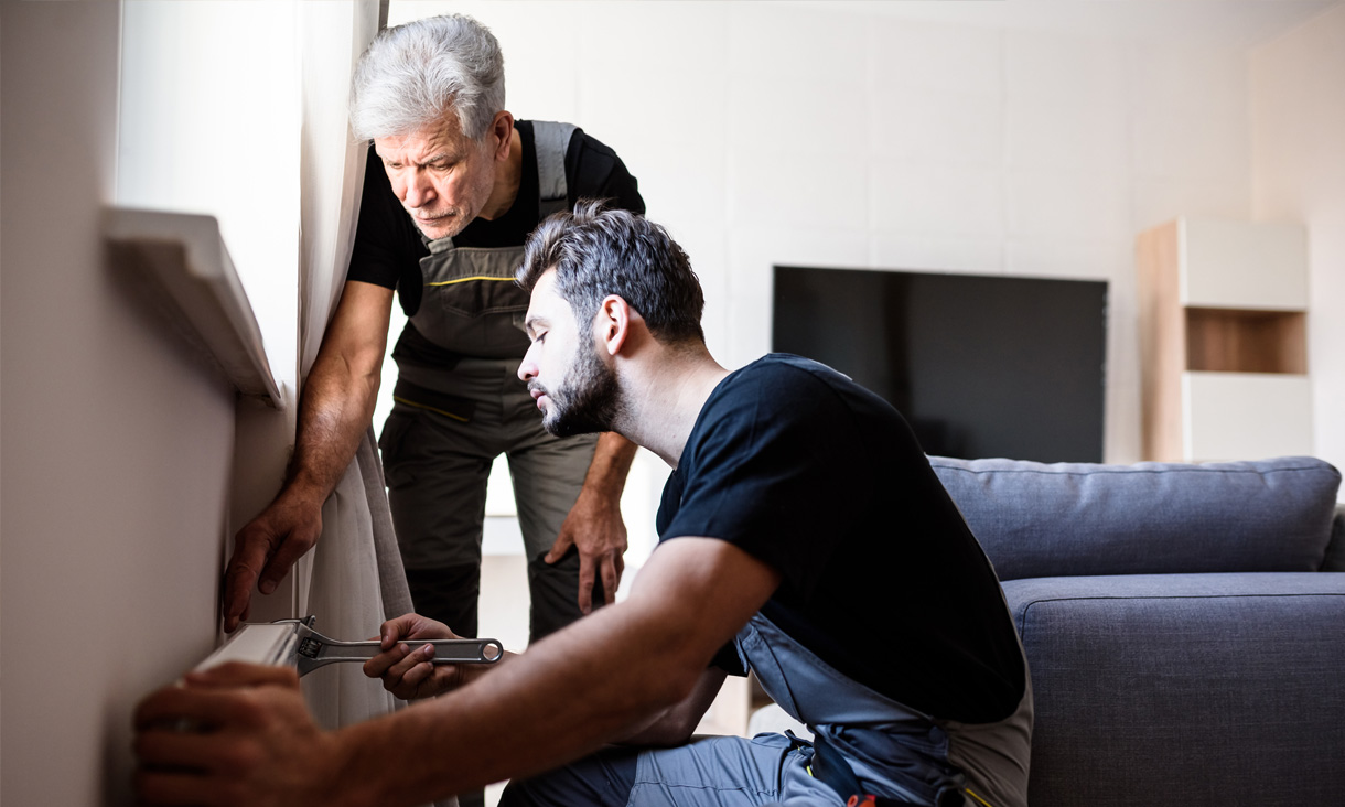 Two plumbers are installing a heater in a living room.