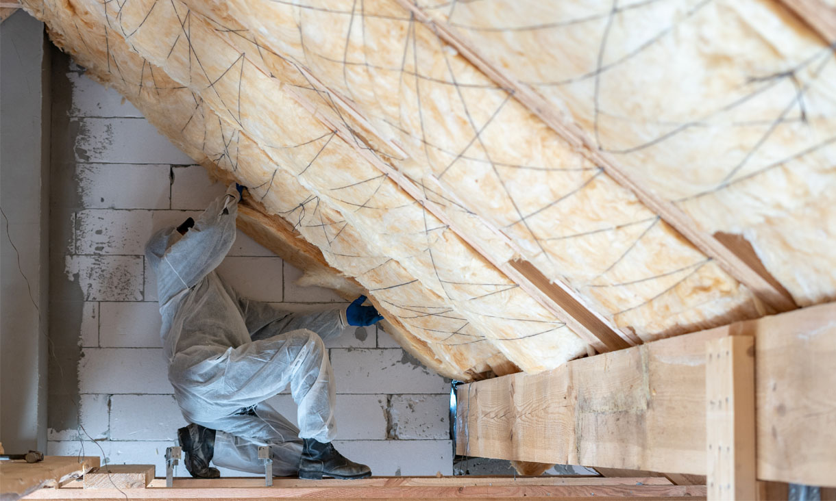 A construction worker installing insulation into the ceiling on a building. 