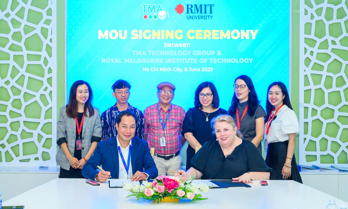 6 people stand behind Mish Eastman and Bui Duc Quang as they sign the MOU