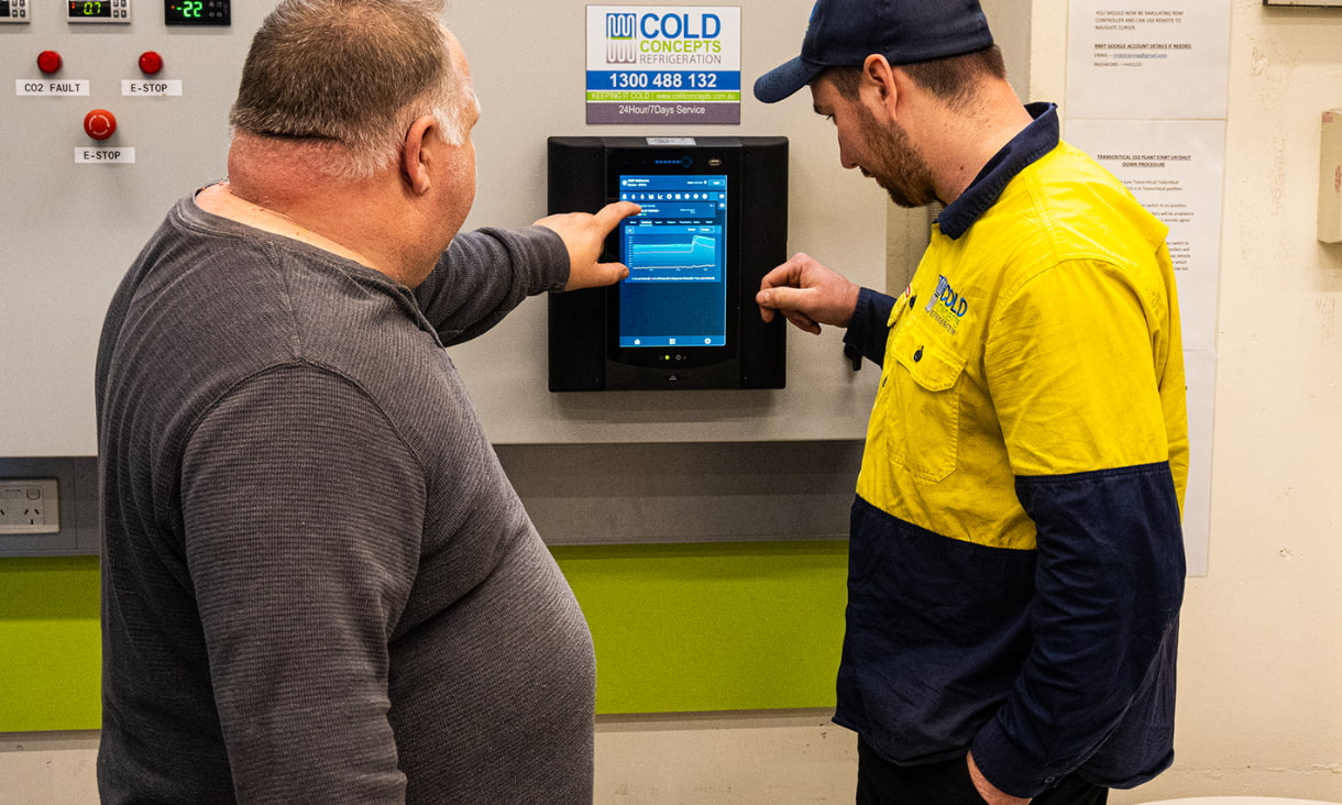 2 men are working with a touchscreen monitor on the wall