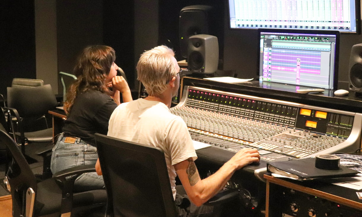 A man and a woman sit at a recording studio desk