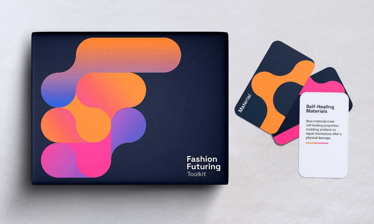 A navy coloured box with an orange colour design. The words "Fashion Futuring toolkit" is on the bottom right side. Next to the box a bunch of cards from the toolkit.