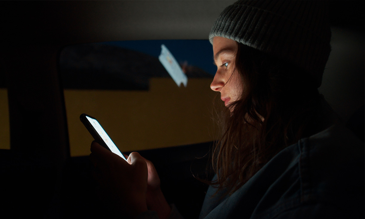 A person scrolling on their phone at night in the backseat of a car.