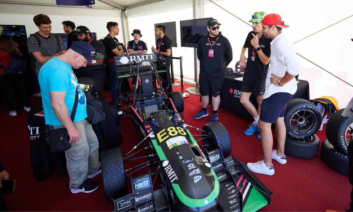 Many people stand around a race car on display.