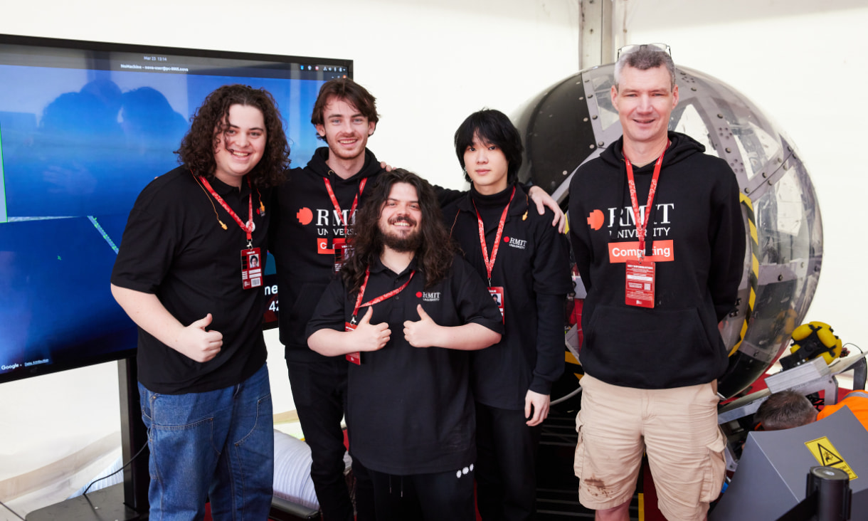 Four students and an academic pose in front of the NOVA Simulator. 