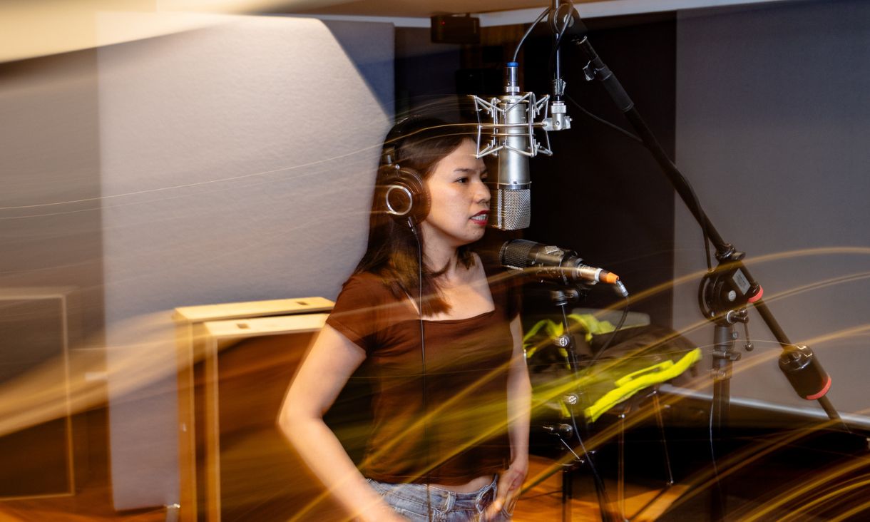 Ahwin in the recording studio, wearing headphones and singing into a microphone.