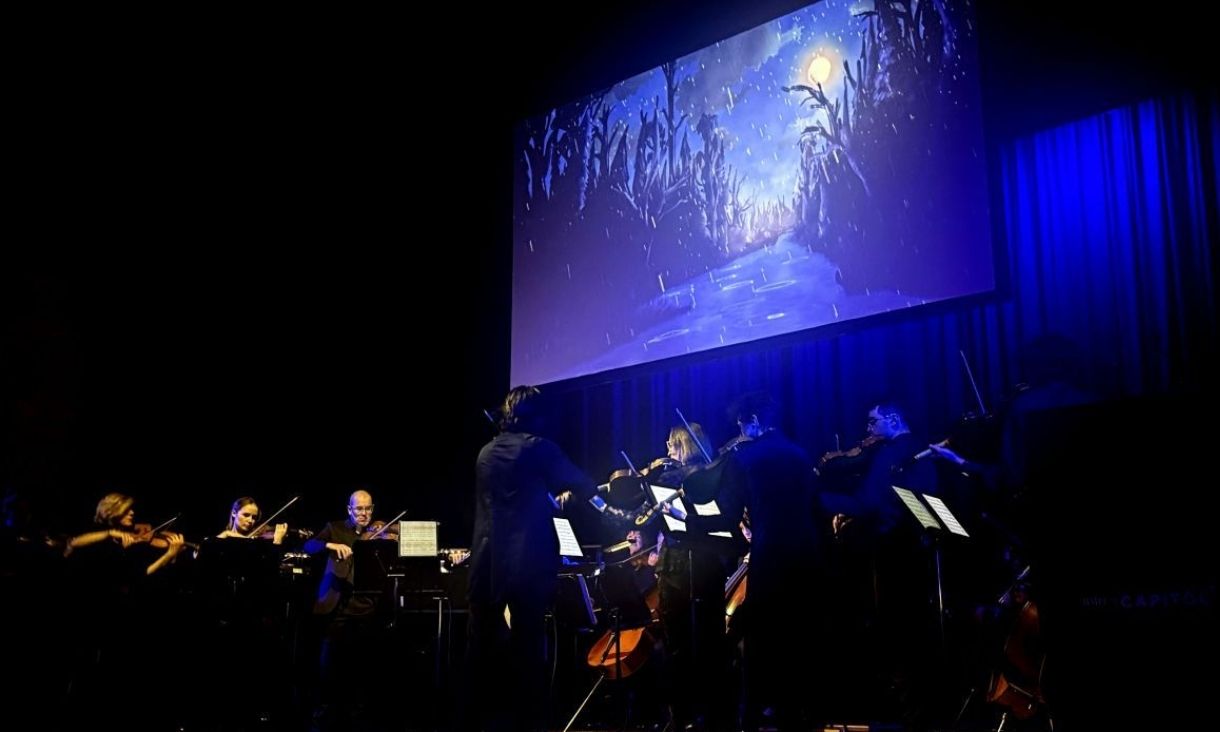 Violinists and other musicians on stage with student animation of a forest at night projected in the background.