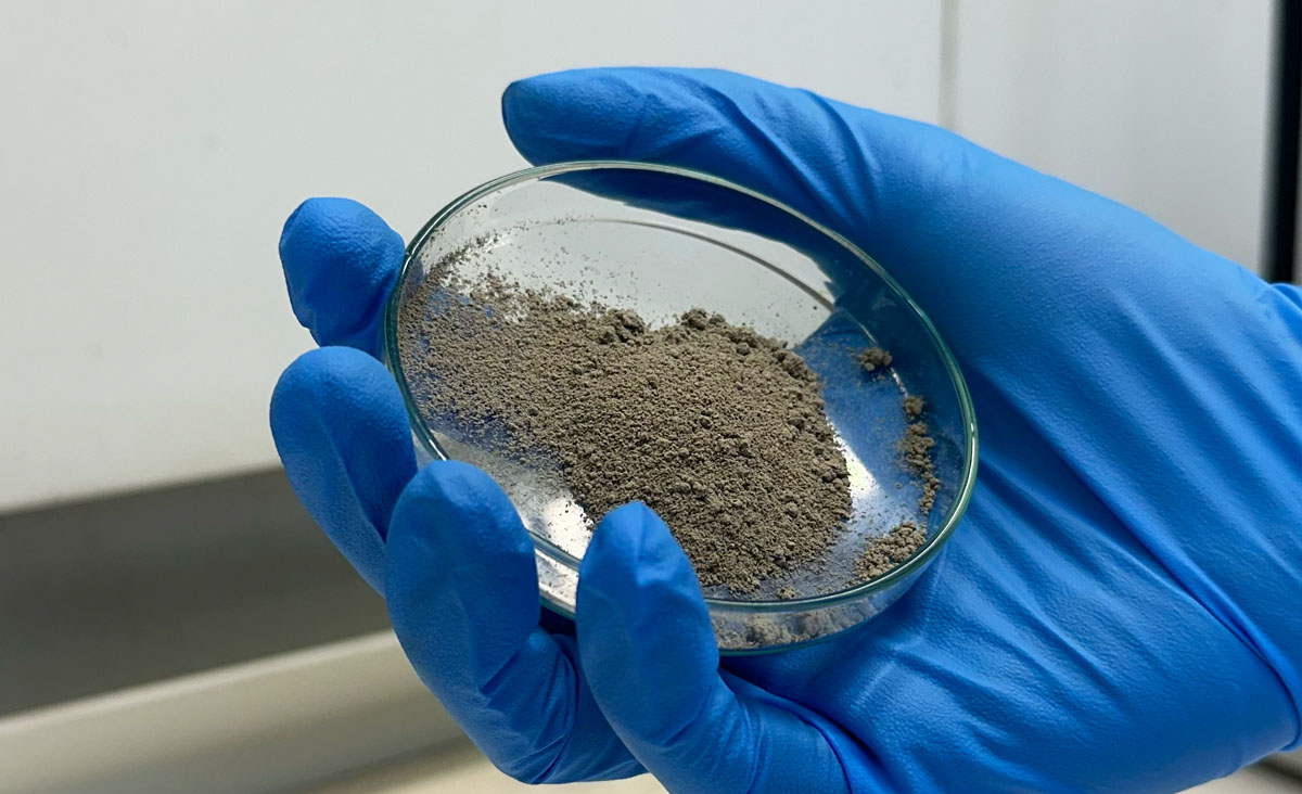 A hand wearing blue disposable gloves is carrying a petri dish of detonated nanodiamond powder.