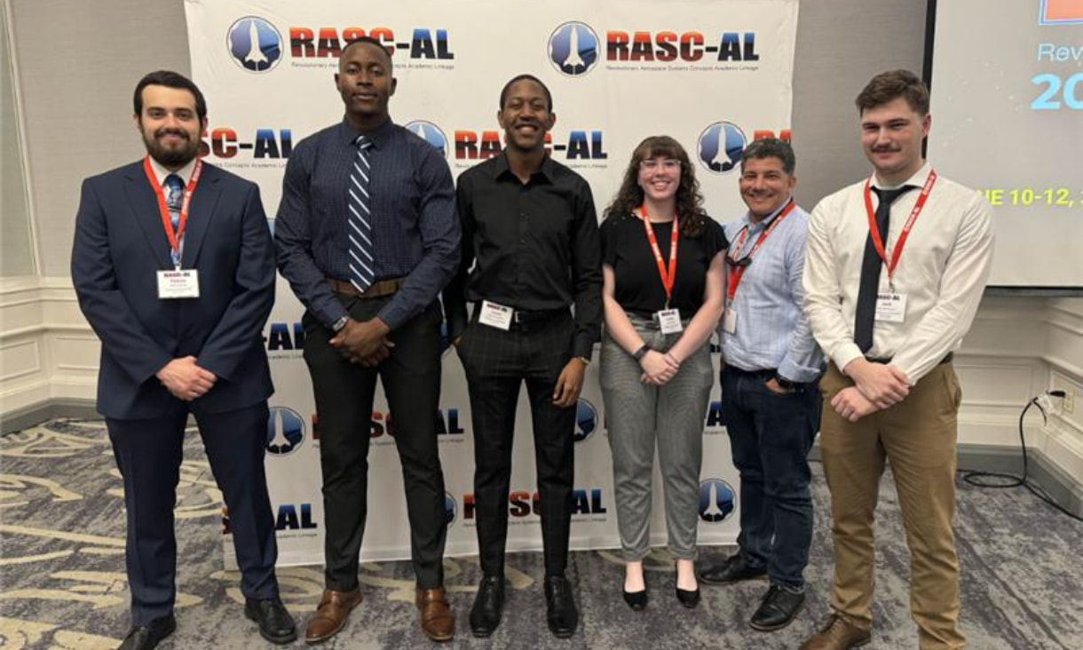 5 men and 1 women standing together in front of a media wall reading RASC-AL.