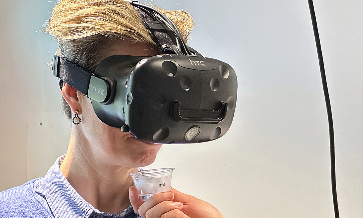 A woman wearing virtual reality goggles and smelling a small container with a cotton bud with an aroma sample, as participants did during the study.