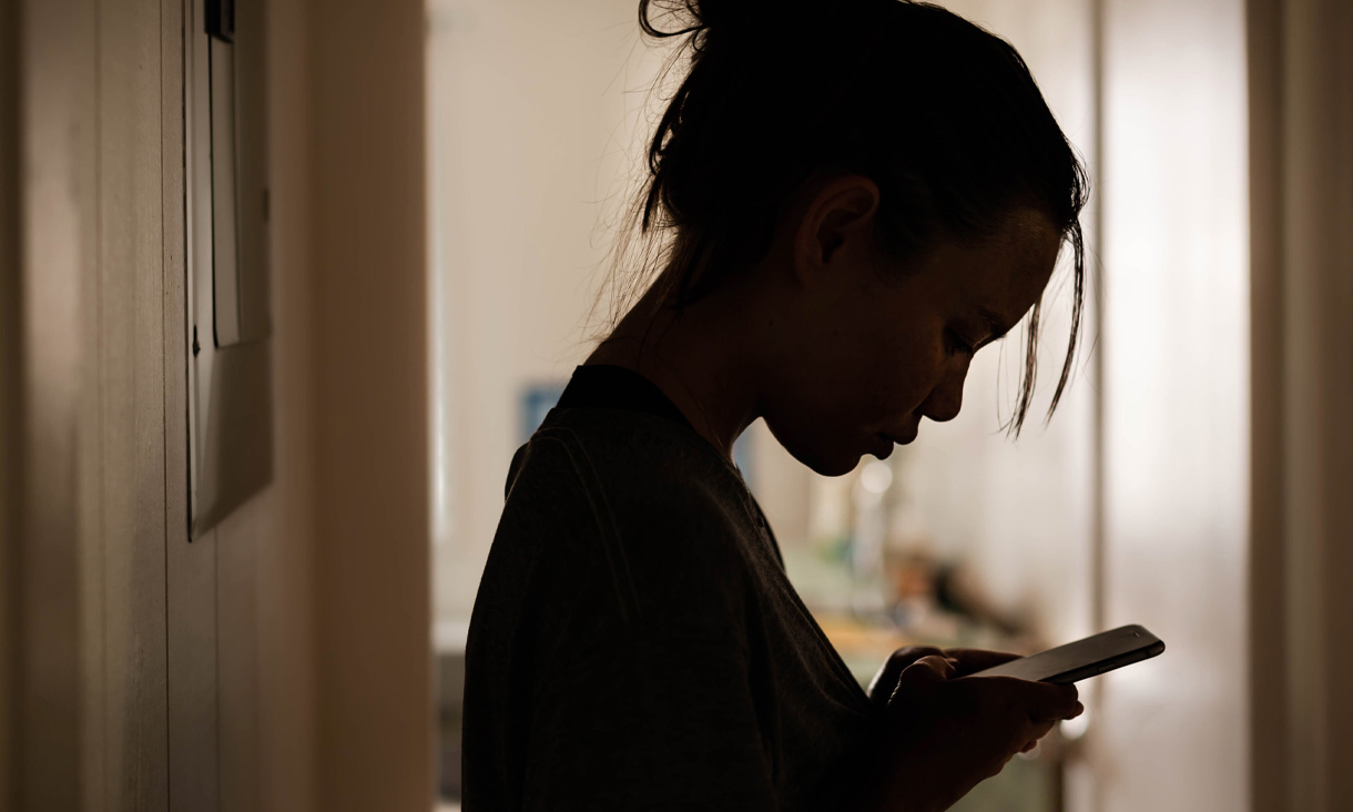 A person standing in a dark room checking messages on their phone. Credit: Adobe Stock