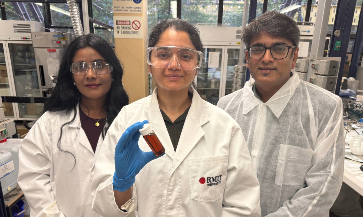 Two women and one man in a lab - the middle person is holding a vile of brown liquid.