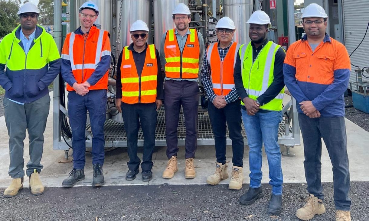 Seven men wearing hard hats and hi-vis clothing at a water recycling facility. 