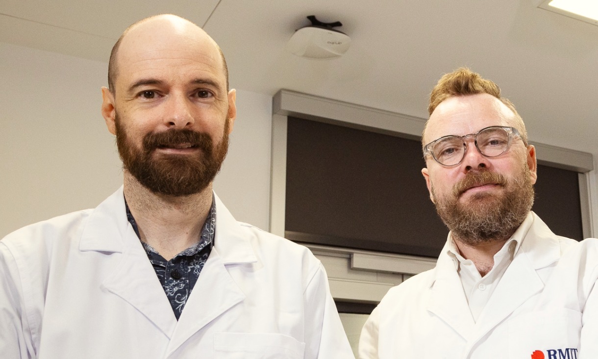 Two male researchers in white lab coats smiling at the camera. 