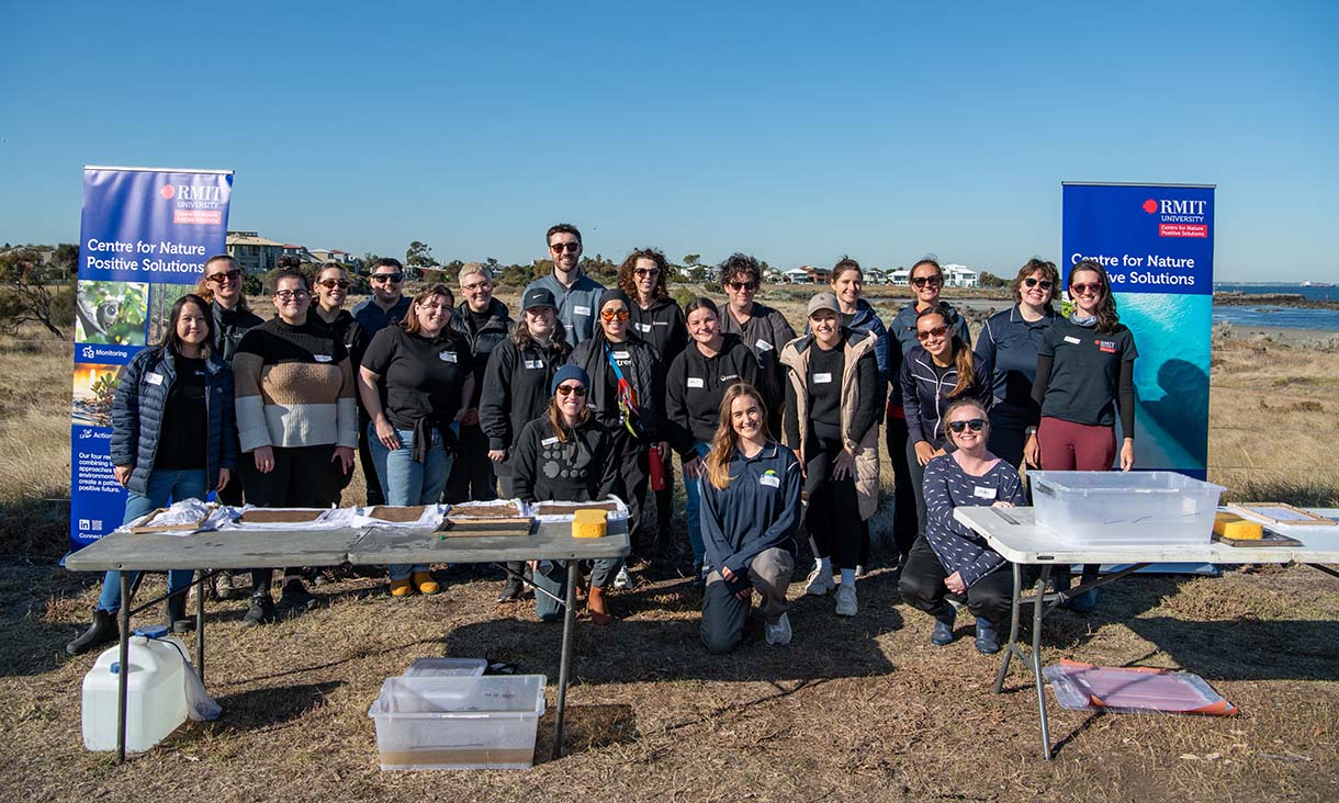 A group of people stands together outdoors with banners from the RMIT Centre for Nature Positive Solutions beside them.