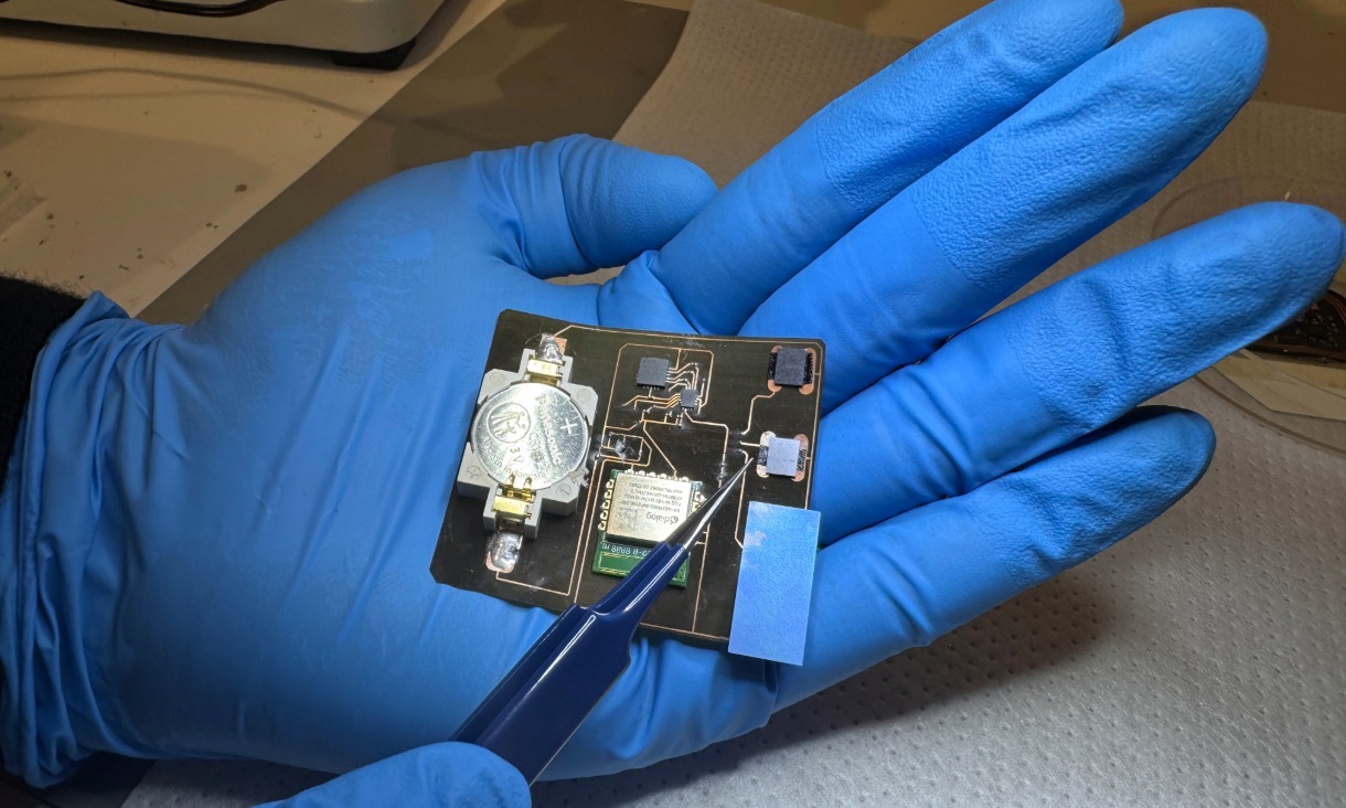 A hand wearing blue gloves holds a compact electronic sensor, developed for monitoring wound healing.