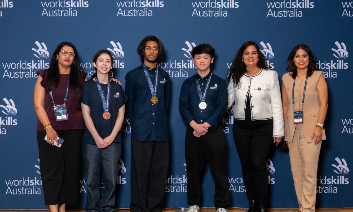 Three competition winners with gold, silver and bronze medals, standing next to three smartly dressed women.