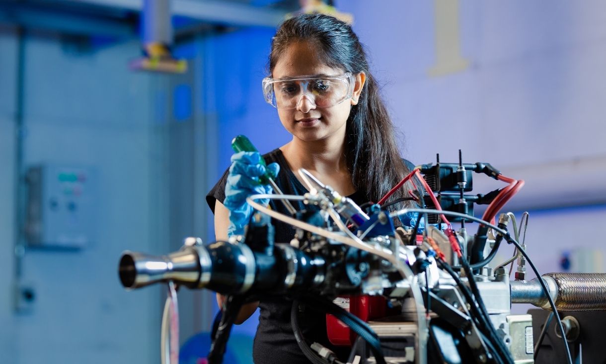 Female student holding screwdriver and examining machine