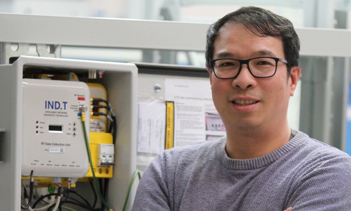 A photo of a man standing in front of a device marked with IND.T..