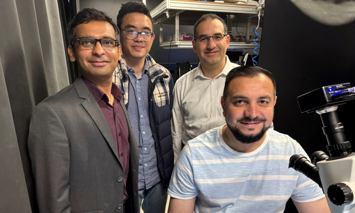 Four men smiling next some lab equipment, including an advanced microscope.