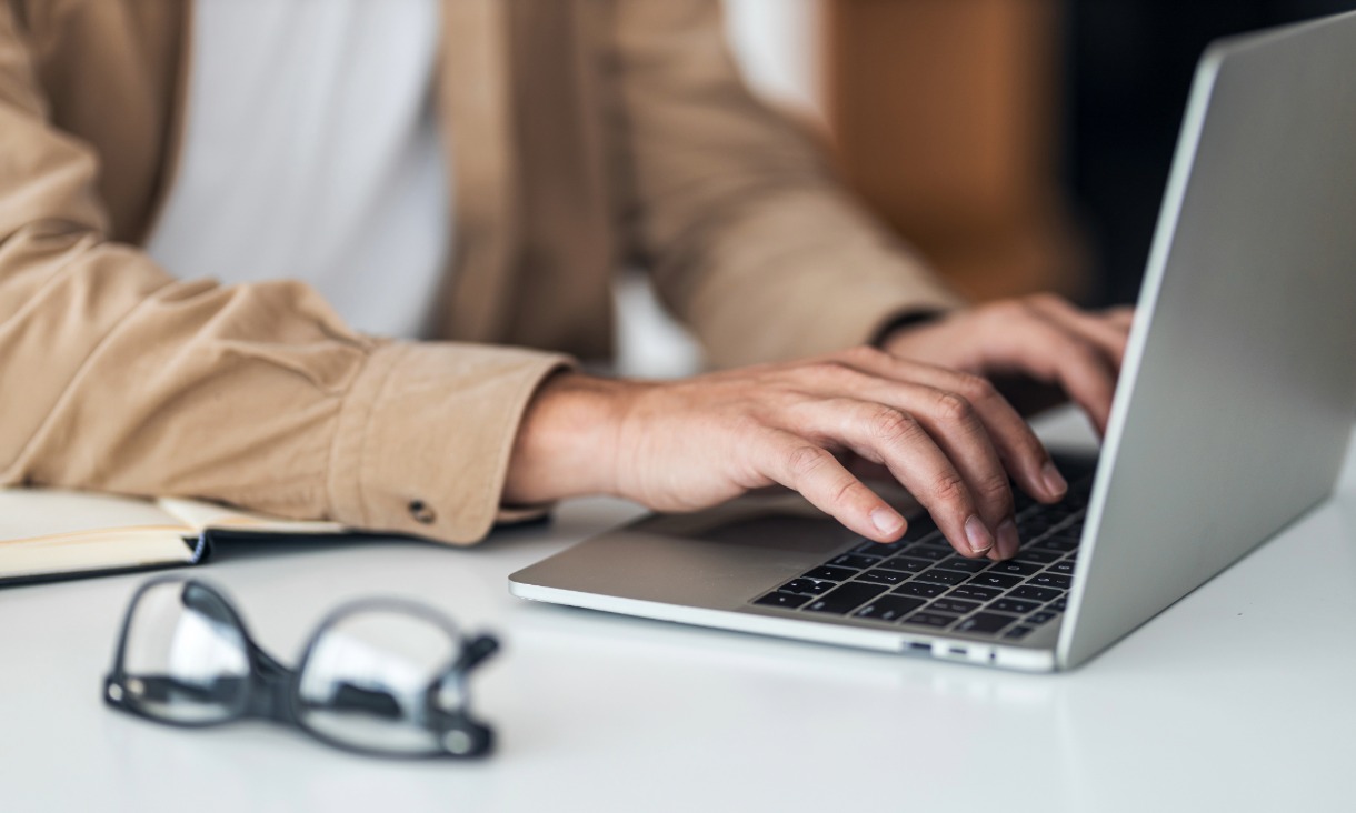 Person typing on a laptop with reading glasses in frame.