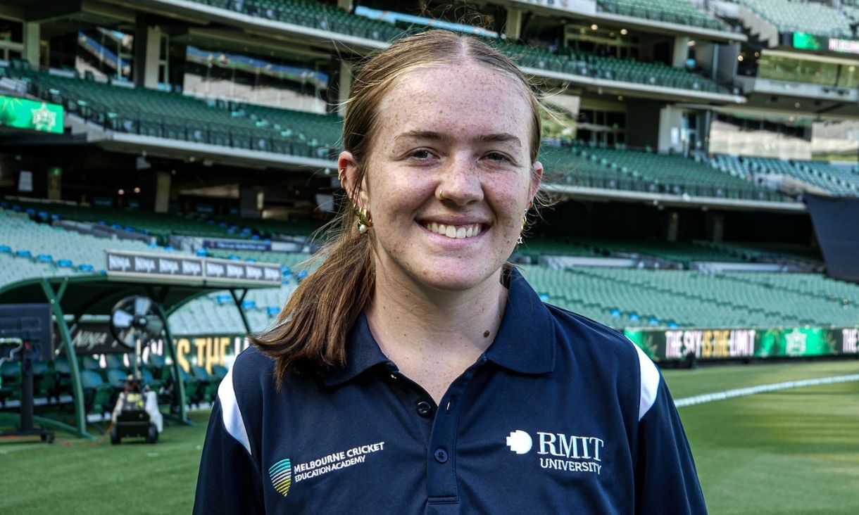 Lily smiles at the camera, she is at a cricket ground
