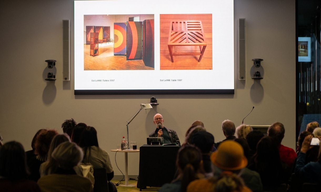 Kaldor showing a slide of photos of wooden furniture and colourful exhibits from the past.