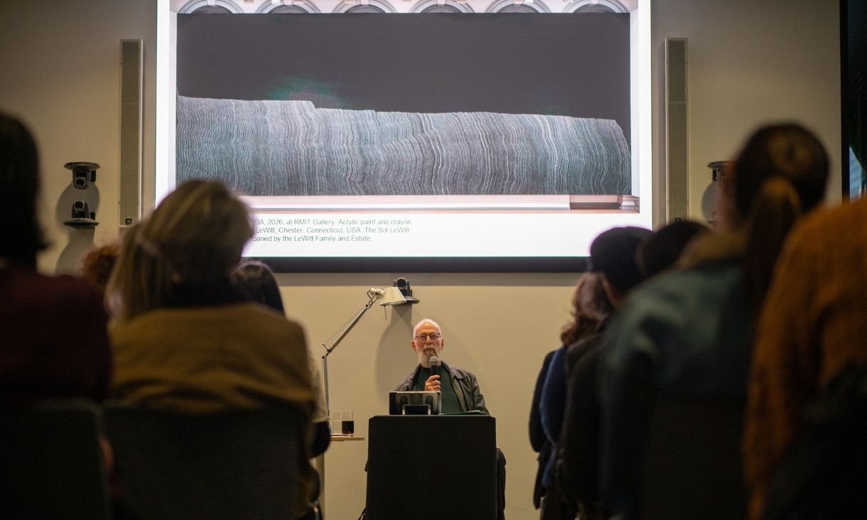 Sol leWitt's wall drawing, lines on a black wall, are being shown by Kaldor on a screen while he speaks to an audience.