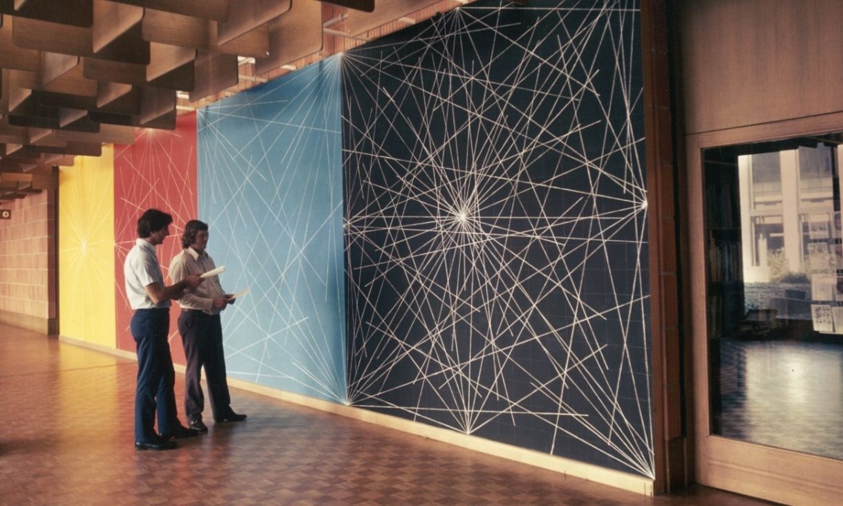 Two men stand together in front of an impressive and colourful wall art