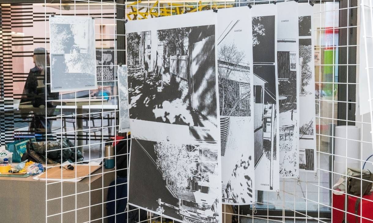 Black and white prints are hung up on a white grate, depicting streets and houses.