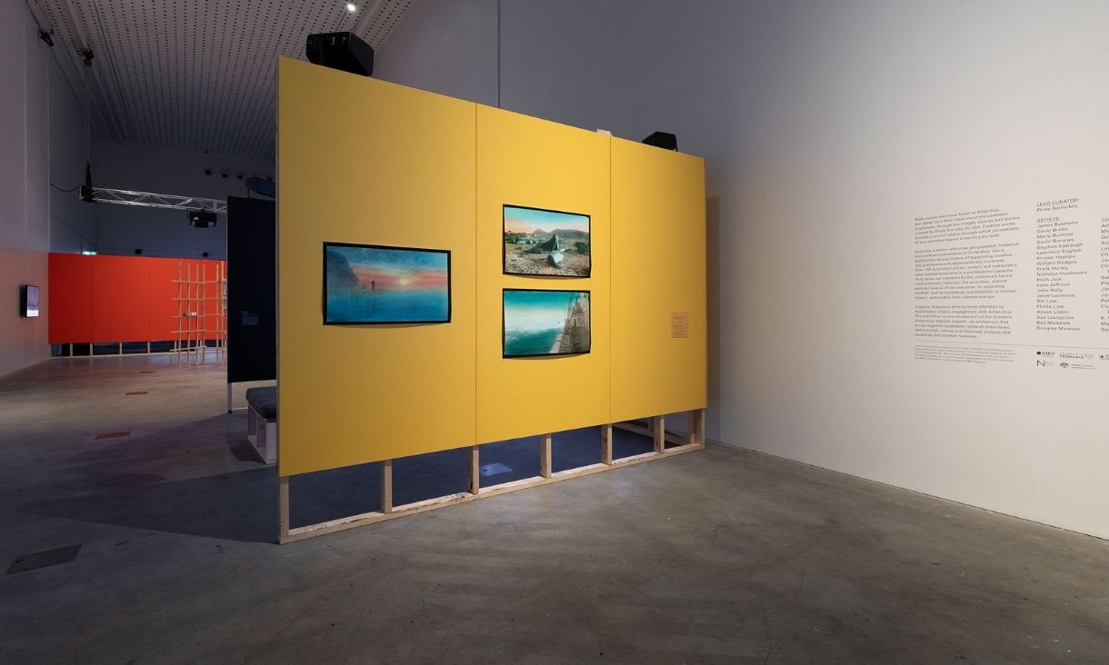 A long shot of the yellow wall, with a red wall backing it in the distance. It has 3 large technicolour prints of the arctic horizon.