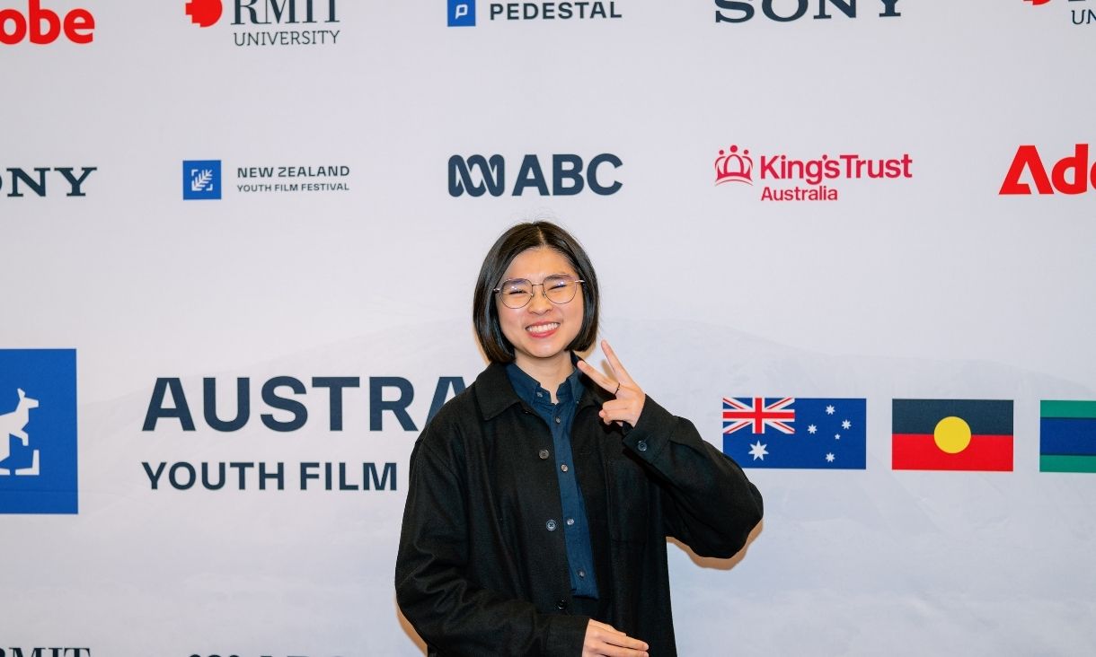 Dai En Ngeiw stands in front of a photo wall, smiling 