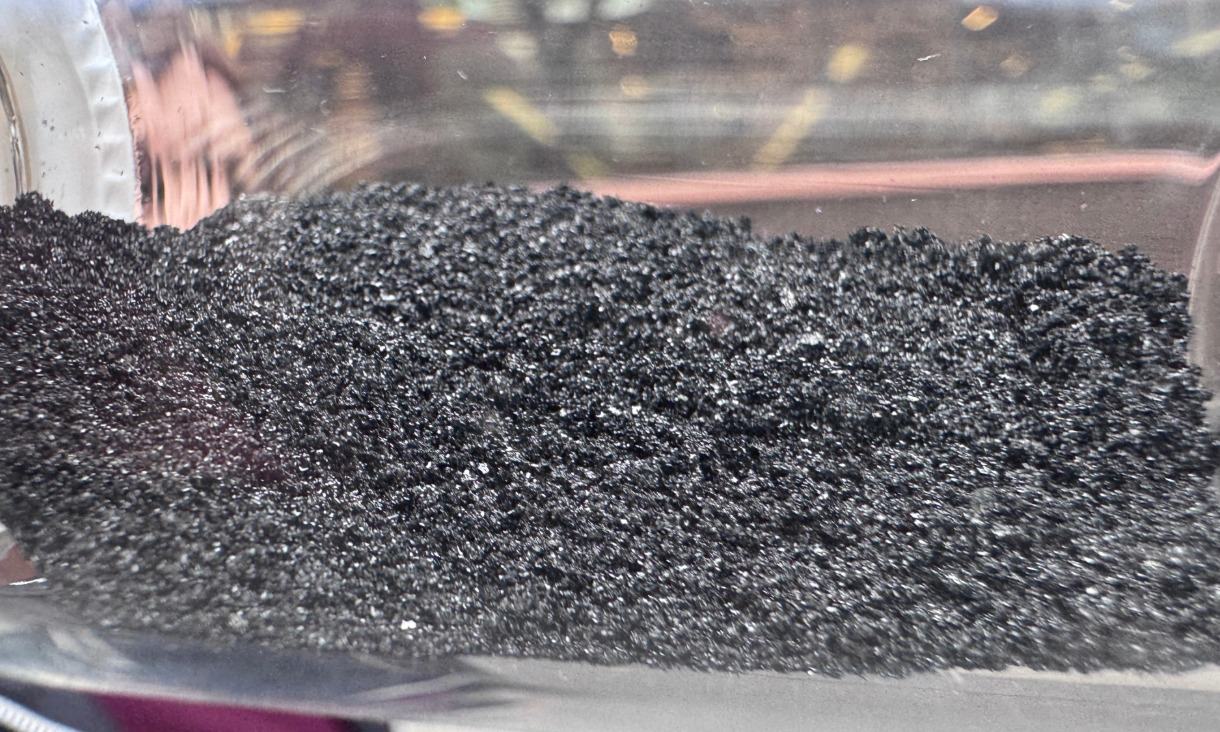 Close-up view of dark granular magnetic adsorbent material inside a transparent container.