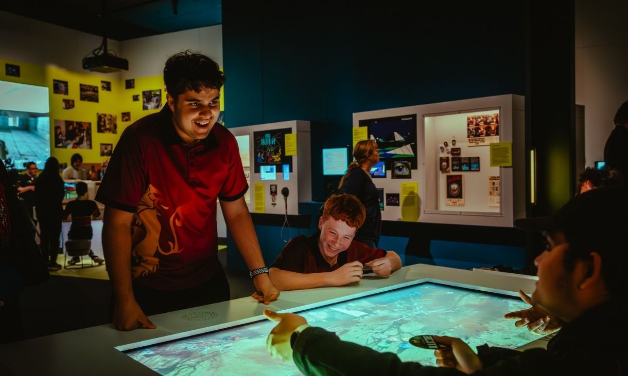 people stand over an interactive display, laughing 