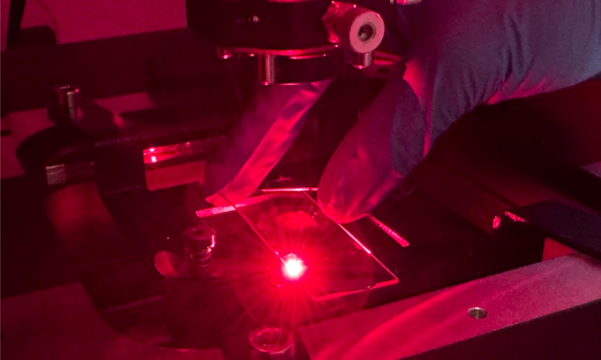Close up of a researcher's gloved hand working inside a nanofabrication machine illuminated with red light, adjusting components within an enclosed chamber used to build and analyse microscopic structures. Credit: Will Wright, RMIT University