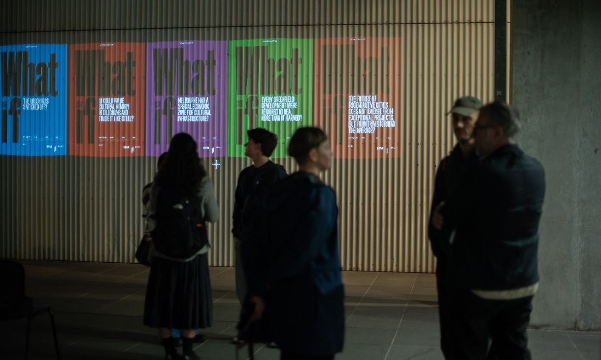 People stand in front of a lit up wall, with individual screens of different colours saying 'What if?' 
