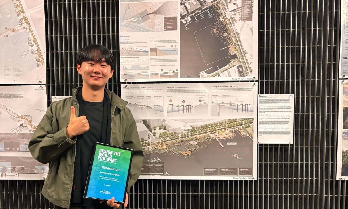 Sunmin stands with the award and with a thumbs up in front of his work 