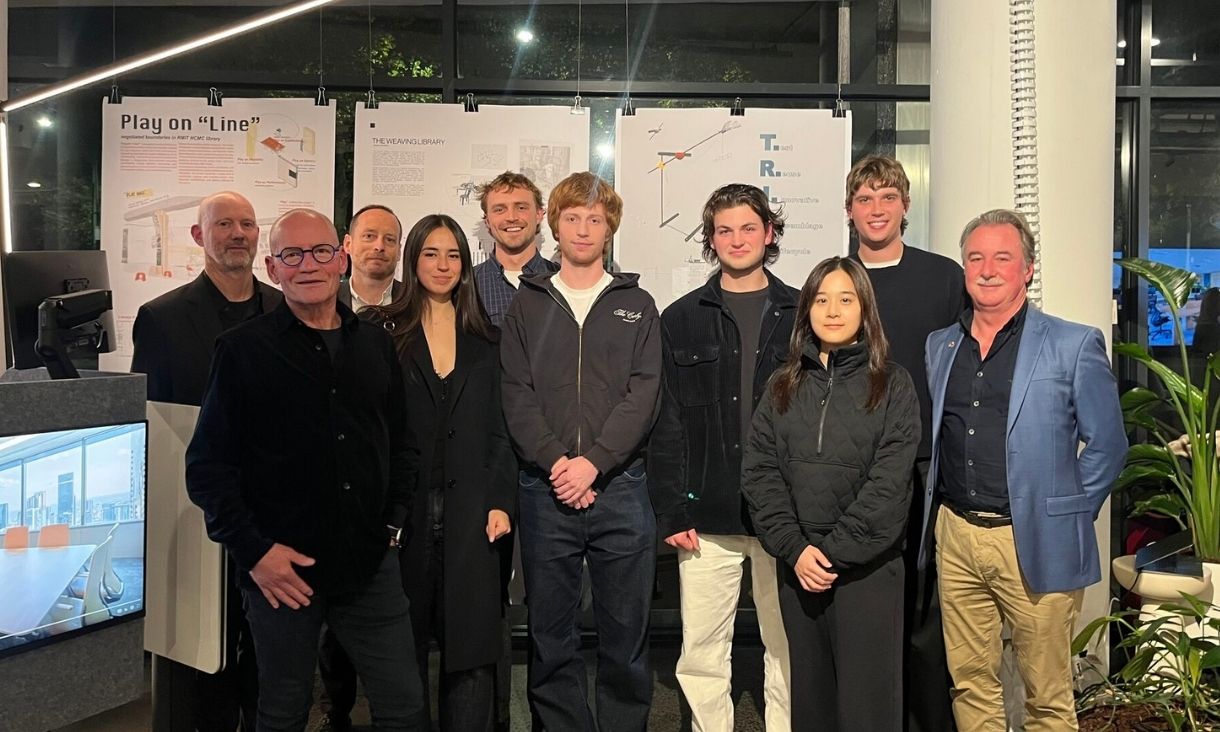 A group of people stand together in a group in front of work being presented.