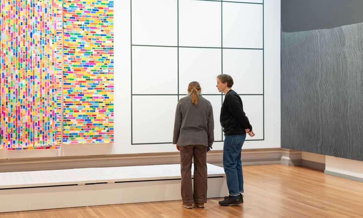 two people stand in front of a bright and large canvas 