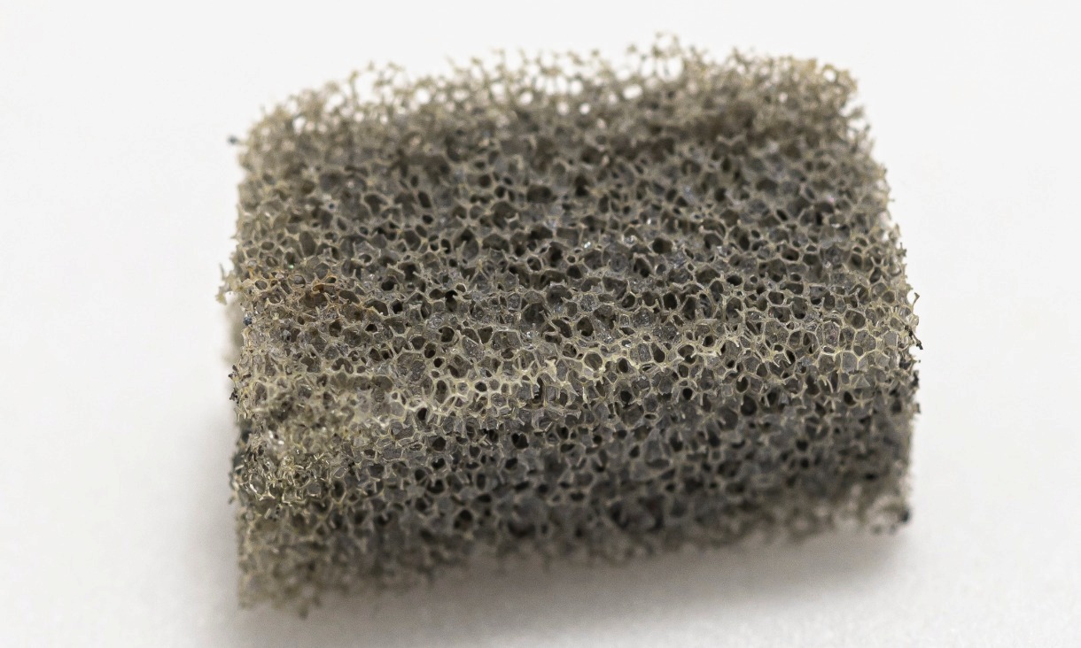 A macro image of a small, porous grey filter sample showing its sponge‑like structure used for oil‑water separation research.