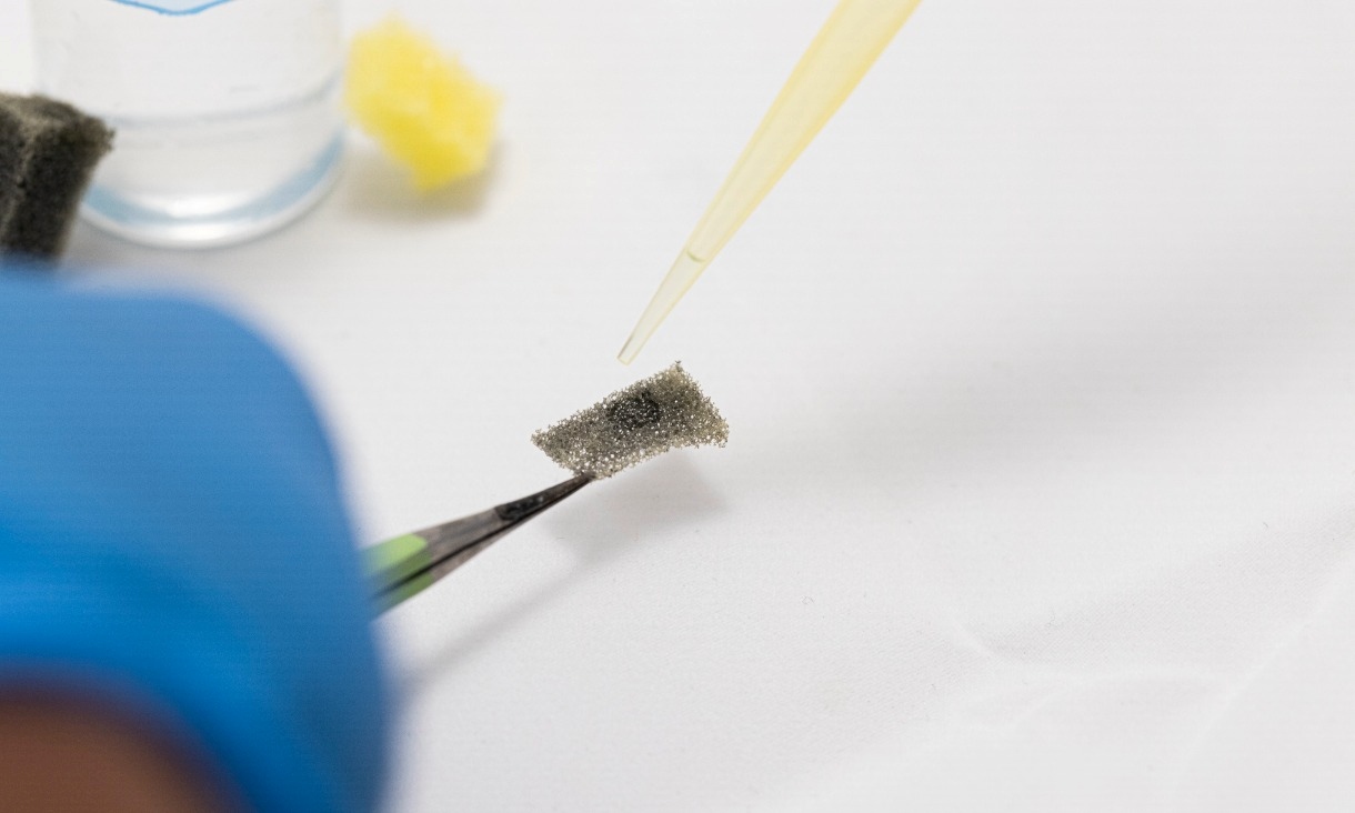A gloved researcher applies a droplet of oil onto the coated filter held by tweezers, showing the material absorbing oil without taking up water.